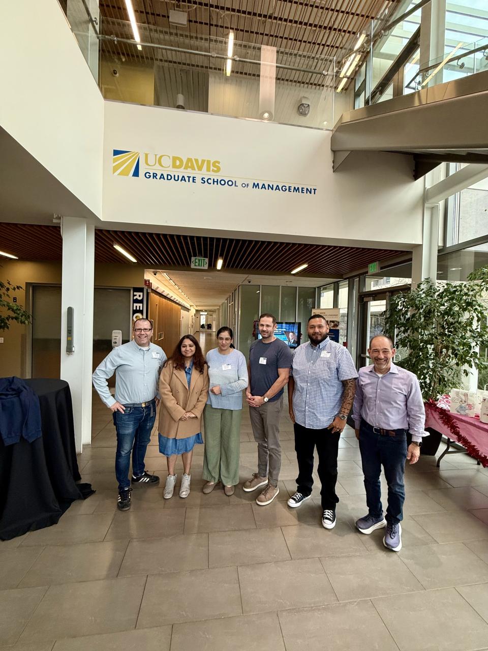 Six people standing and smiling in the lobby of the UC Davis Graduate School of Management.