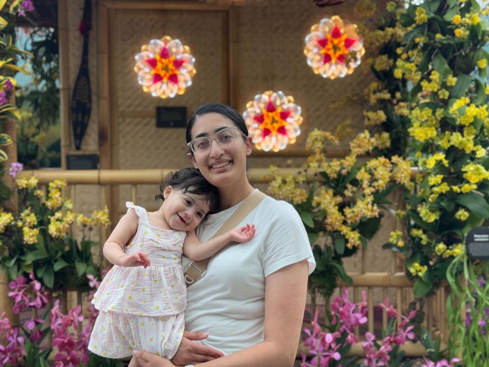 An adult and a young child pose together in front of a bamboo wall decorated with flowers and illuminated hanging ornaments.
