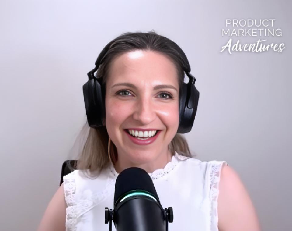 Woman wearing headphones and a white top speaks into a microphone against a light background with the text “PRODUCT MARKETING Adventures” in the top right corner.