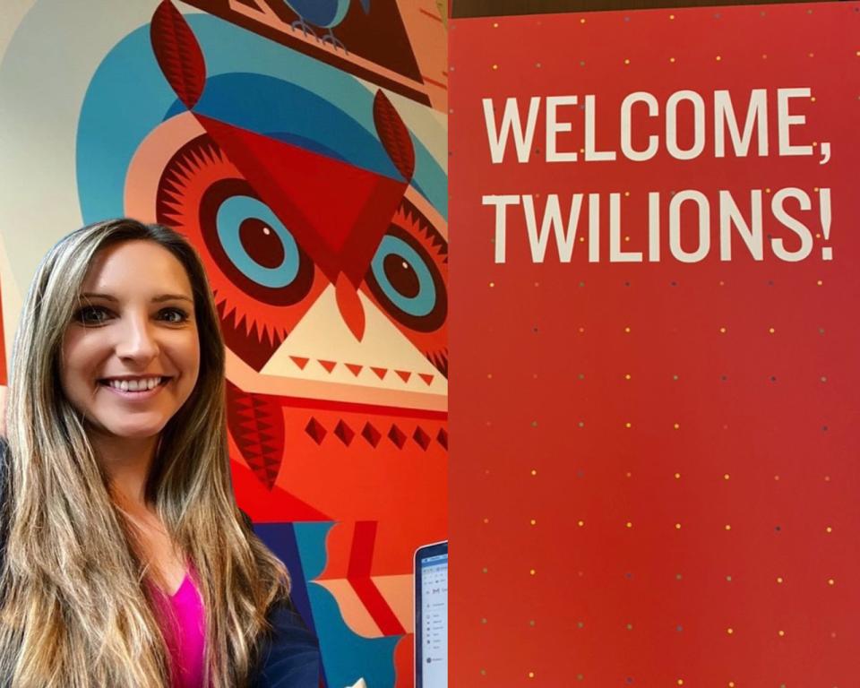 Woman smiling next to a colorful owl mural and a red sign that reads "WELCOME, TWILIONS!
