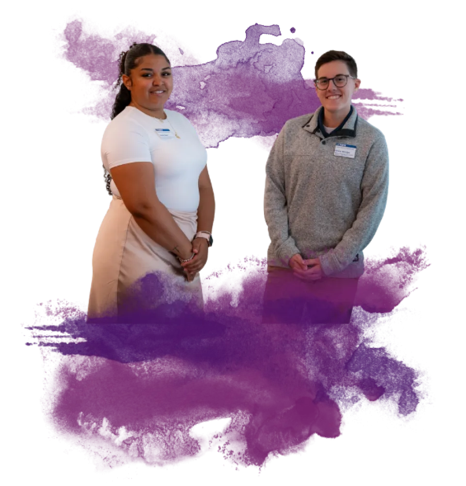 Two people stand side by side in front of a white background with a purple paint splash behind them. Both wear name tags and smile at the camera.