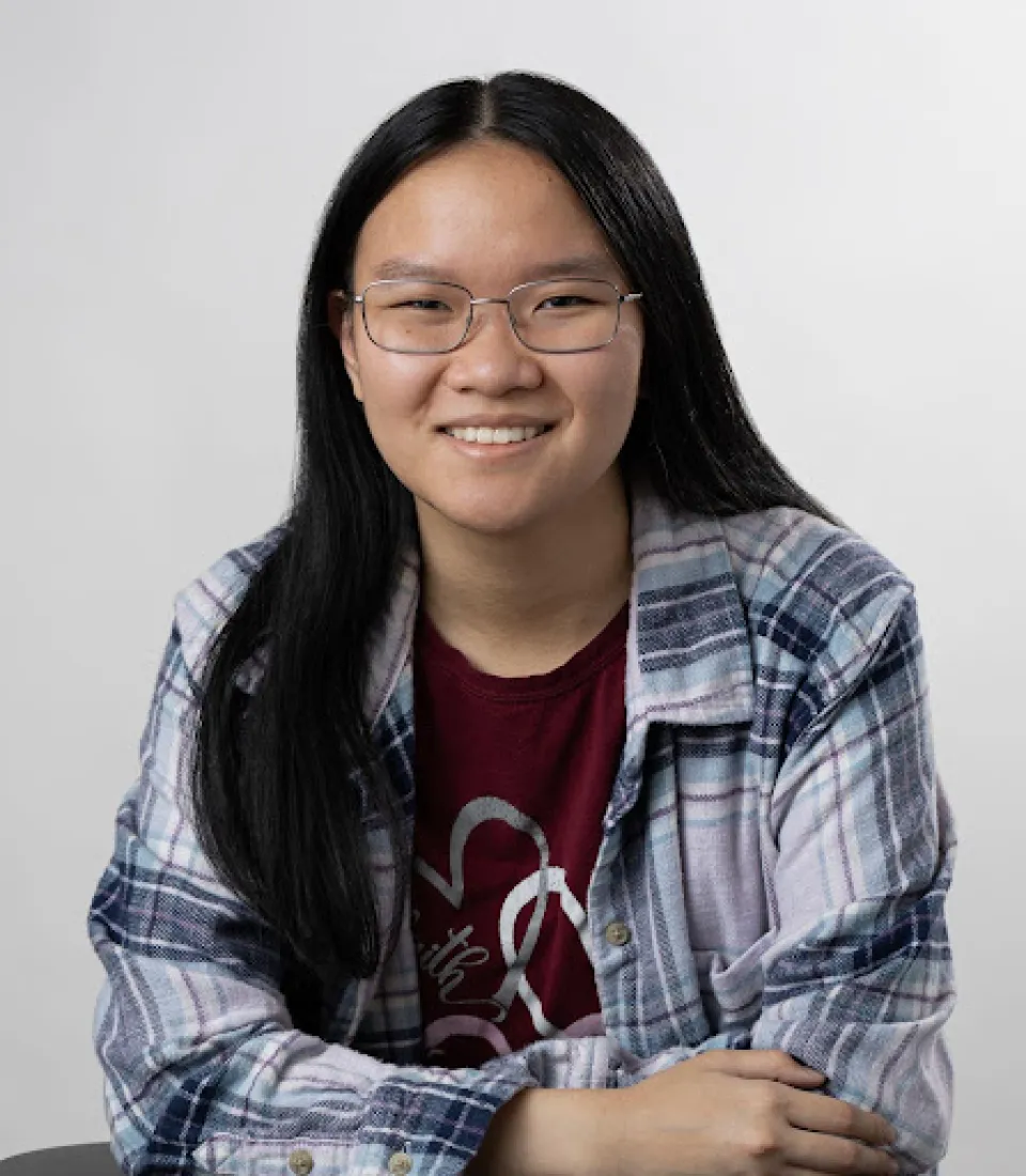 Alinda Lau sits smiling with arms crossed on a table against a plain light background.
