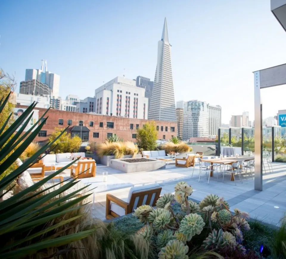 Rooftop patio with seating and plants overlooking downtown San Francisco, featuring the Transamerica Pyramid and other tall buildings in the background.