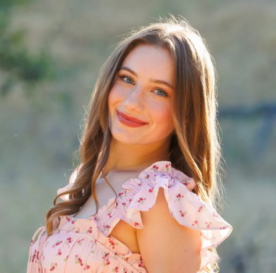 Brooke Barson stands outdoors, smiling at the camera with a blurred natural background.