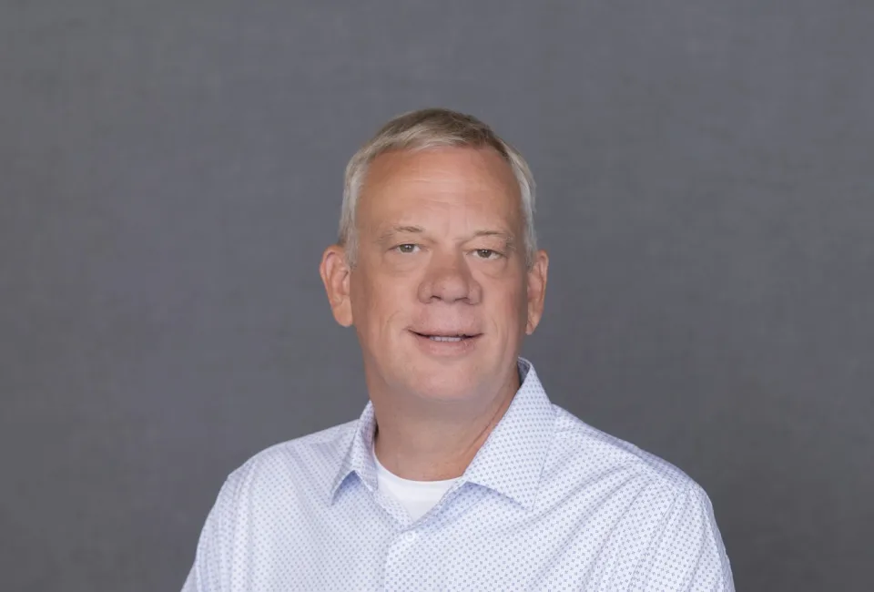 Benjamin Coss wearing a white button-up shirt, posing in front of a plain gray background.