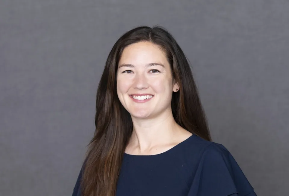 Suzanne Howar wearing a navy blouse, smiling in front of a plain gray background.