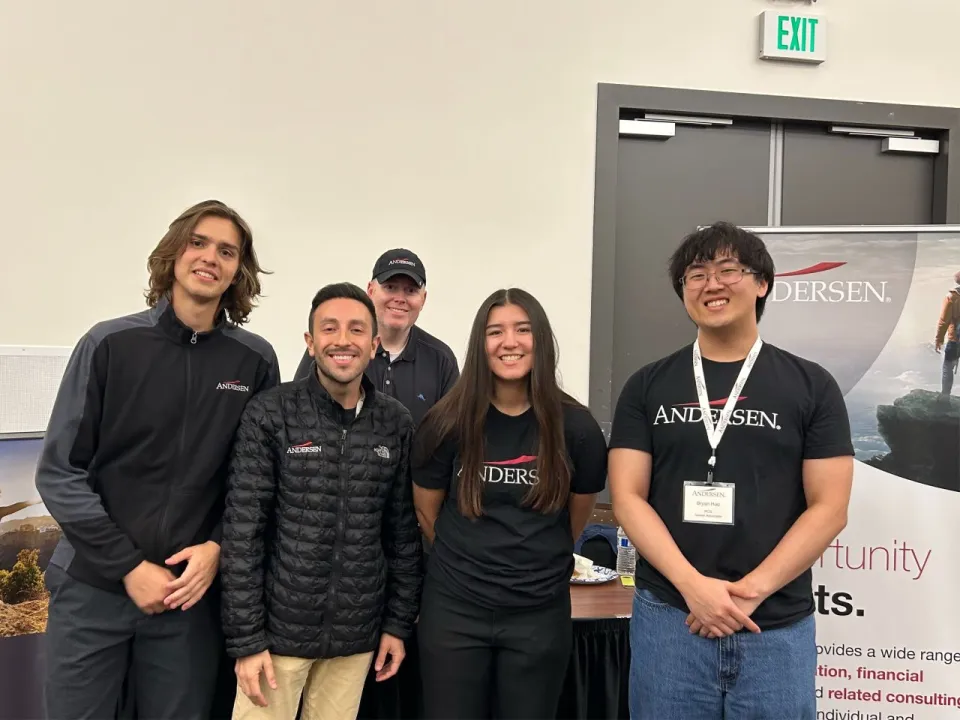 Five people in Andersen-branded apparel standing in front of an Andersen recruitment banner.