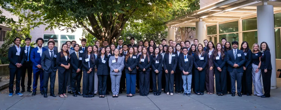 A large group of students in professional attire posing for a photo outdoors in front of a building.