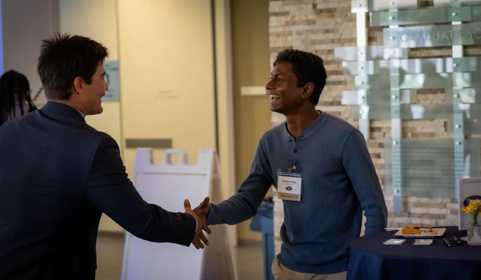 Two men shaking hands and smiling at a networking event.
