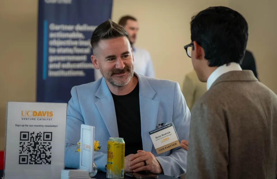 A group of people networking at a professional event, some wearing name tags and holding papers.