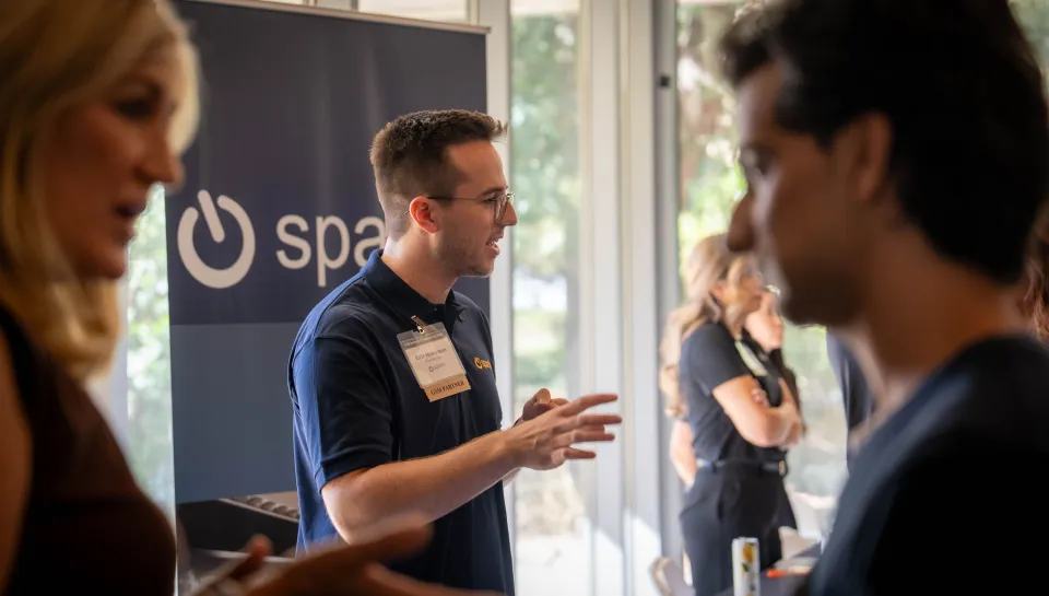 A group of people networking at a professional event, some wearing name tags and holding papers.