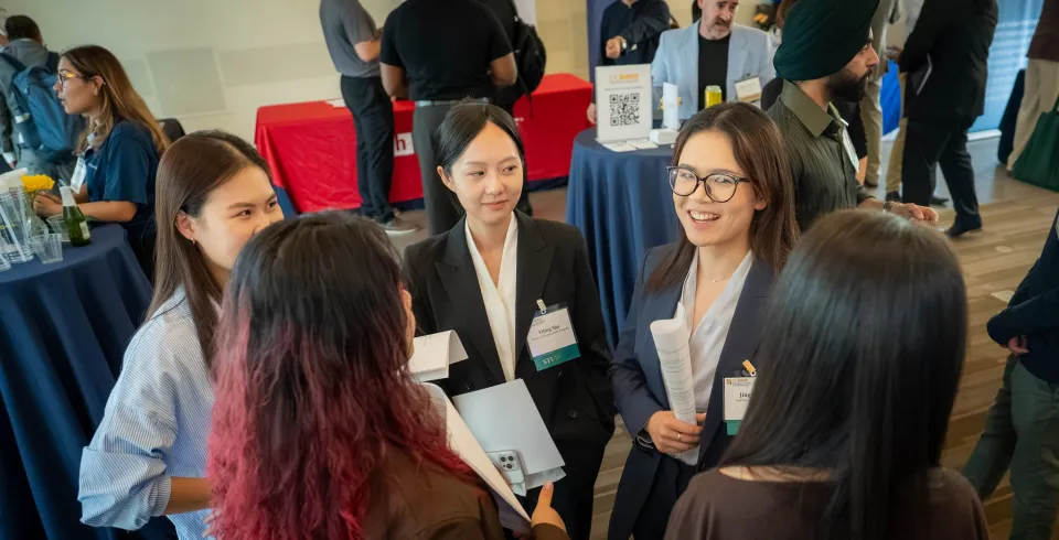 A group of people networking at a professional event, some wearing name tags and holding papers.