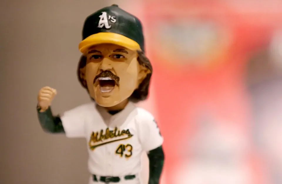 A bobblehead figurine wearing an Oakland Athletics baseball uniform and cap, with mouth open and right fist raised.