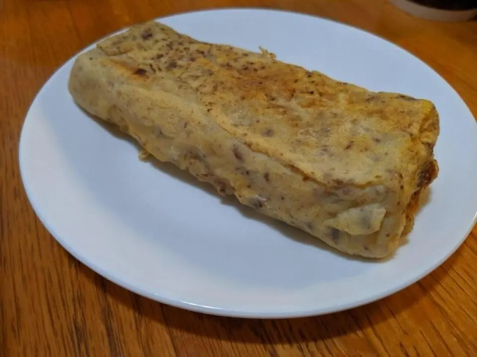 A rectangular rolled omelette is placed on a white plate set on a wooden table.