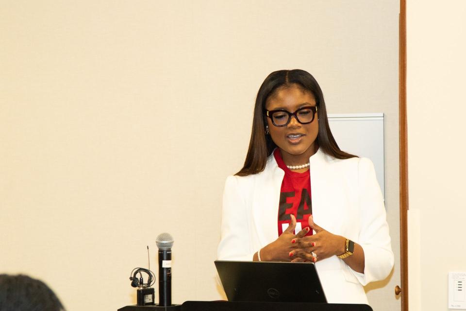 Shaneil McKenzie-Guyher at a podium, reading off a laptop