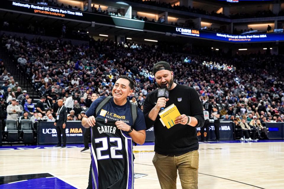 Eddie Ramirez standing on the Sacramento Kings court, holding up a basketball jersey