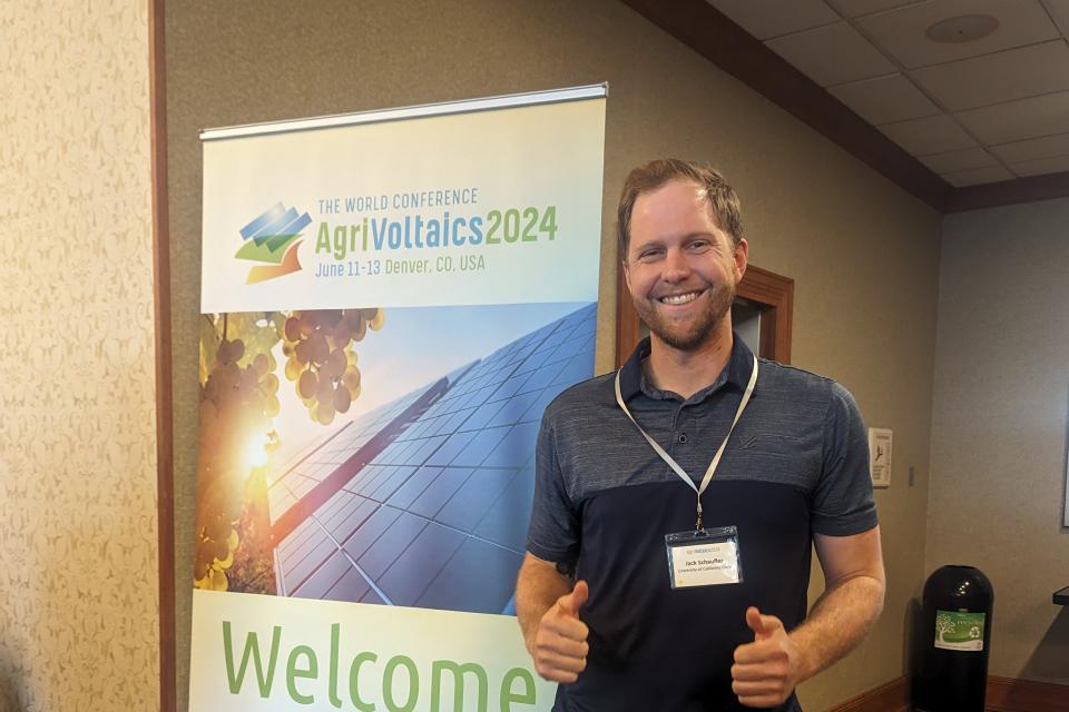 Jack Schauffler holding up two thumbs up, standing next to a welcome sign at a conference