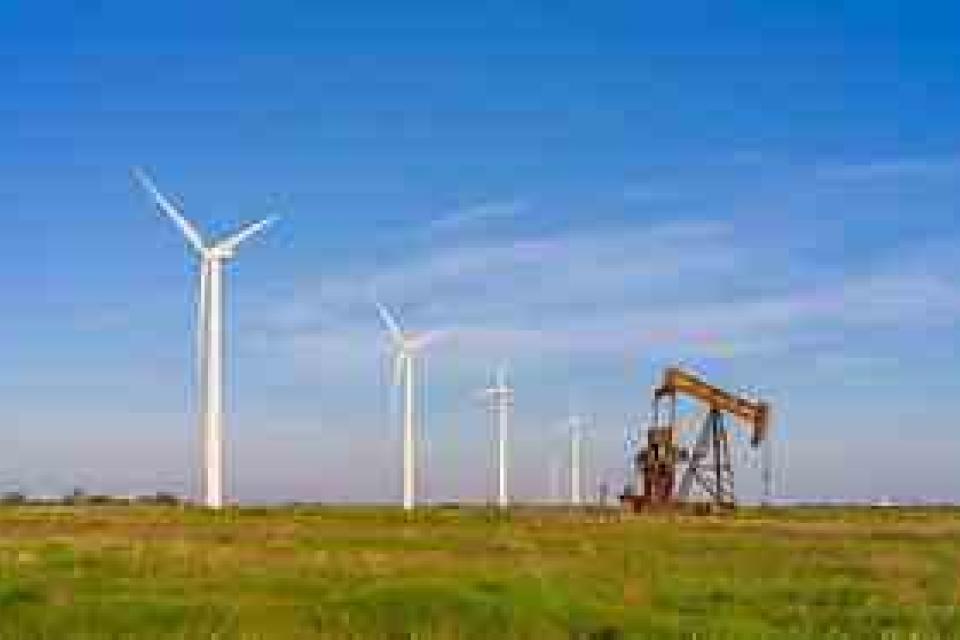 Wind turbines and an oil pumpjack stand side by side in a grassy field under a clear blue sky, symbolizing the contrast between renewable energy and fossil fuels.