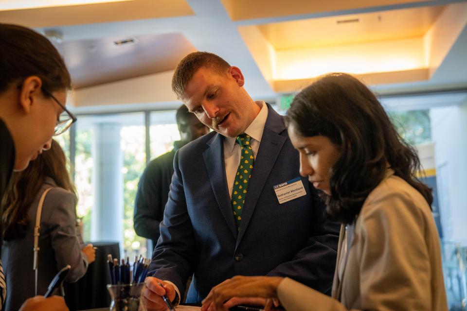 Nathaniel Wentland in a suit at Gallagher Hall, talking to other MBA students