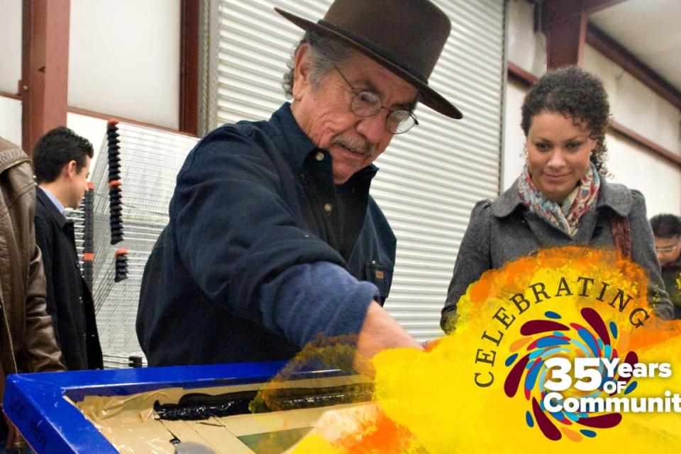 A group of people participate in a hands-on screen-printing activity in a workshop space. An older man wearing a hat demonstrates the process while others look on and smile. A colorful graphic overlay reads “Celebrating 35 Years of Community.”