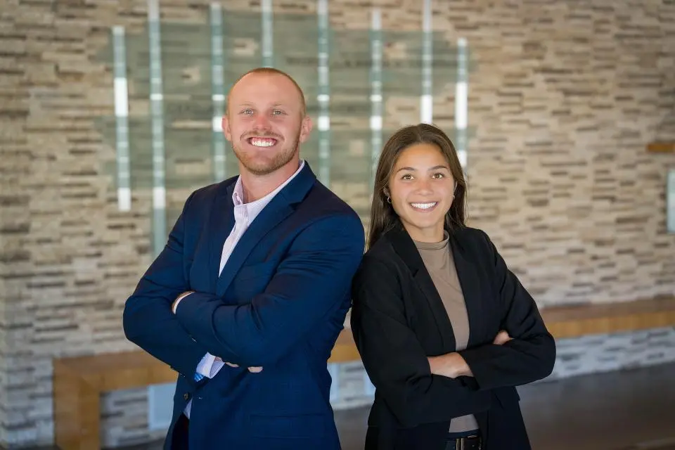 Two students standing back to back with their arms crossed, smiling at the camera