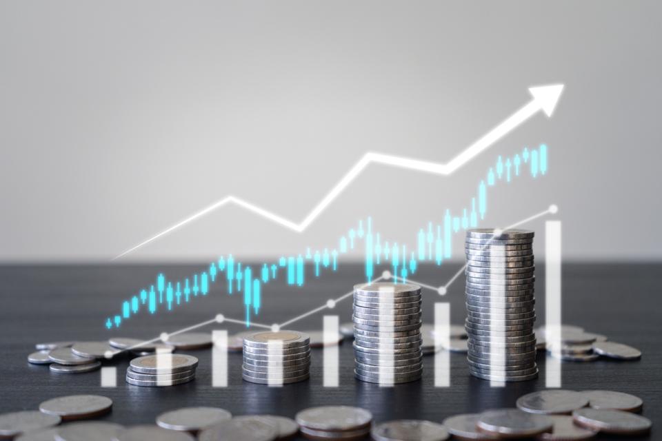 Stacks of coins in ascending order with a white upward-pointing arrow and bar graph overlay, symbolizing financial growth or increasing profits.