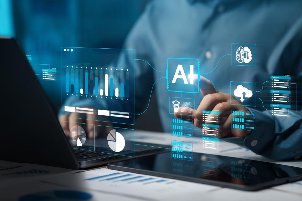 Person using a laptop and tablet, interacting with virtual AI-themed data graphics and analytics charts projected in the air.