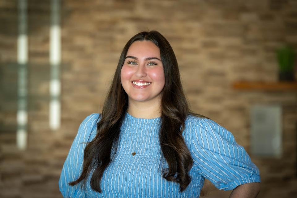 Lizzie Loredo stands smiling in front of a blurred brick wall background.