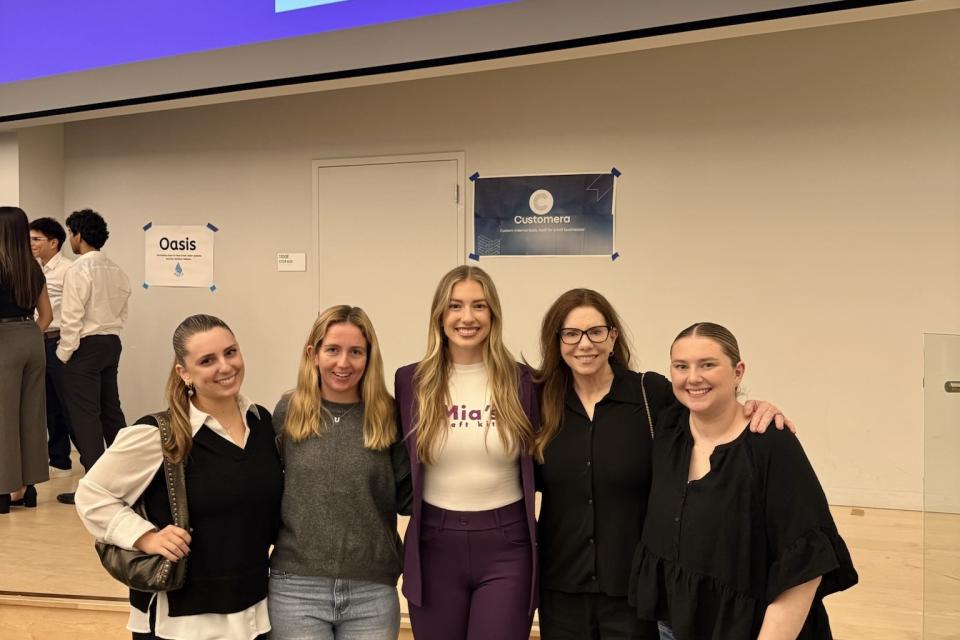Five women stand together smiling in front of a presentation screen displaying a large QR code and a cartoon pig.