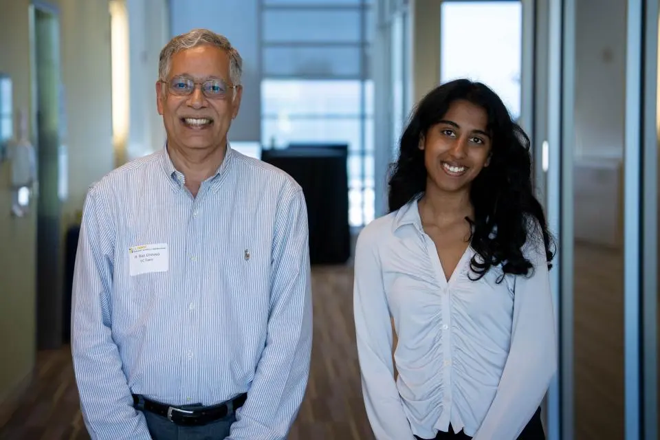 Dean Unnava and Rachel Johnson side by side in a hallway, both wearing light-colored shirts and smiling at the camera.