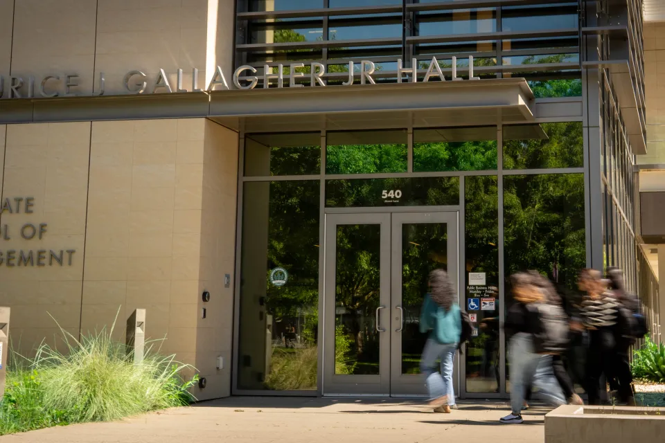 Students walk past the entrance of Maurice J. Gallagher Jr. Hall, Graduate School of Management, on a sunny day.