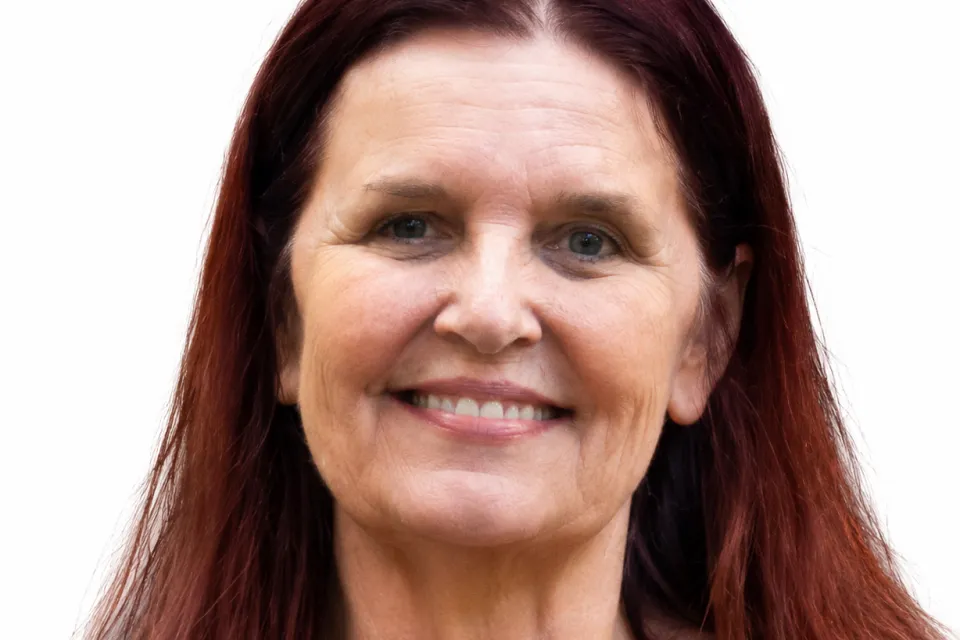 A woman with long reddish-brown hair and light skin smiles at the camera against a plain white background.