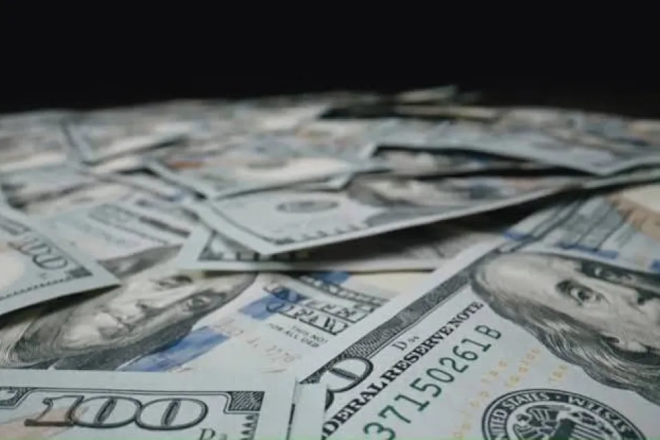 A pile of scattered United States one hundred dollar bills, showing Benjamin Franklin’s portrait and various security features.