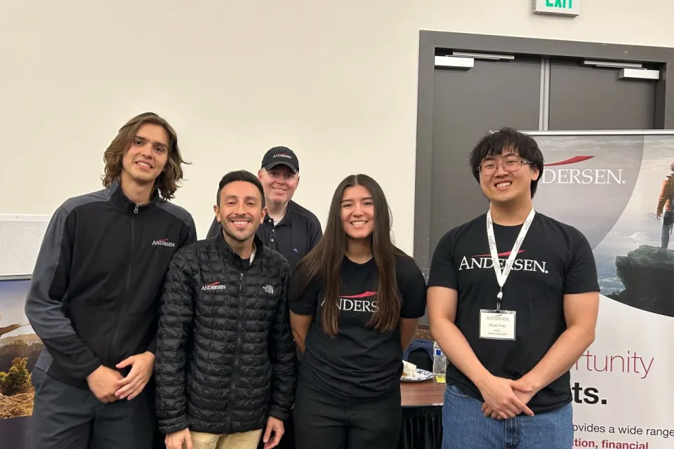 Five people in Andersen-branded apparel standing in front of an Andersen recruitment banner.