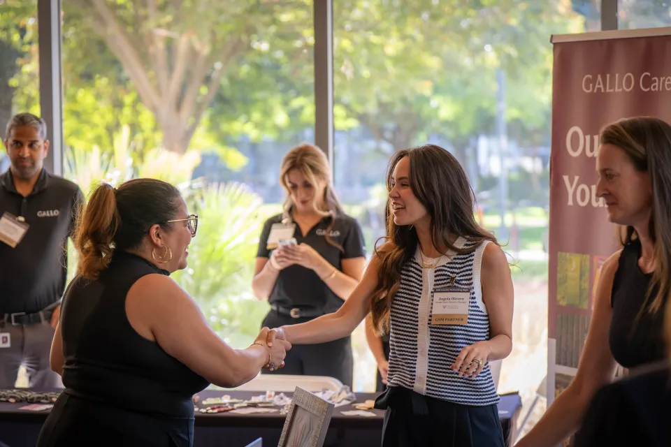 Two women shaking hands at a career fair booth branded with Gallo Careers.